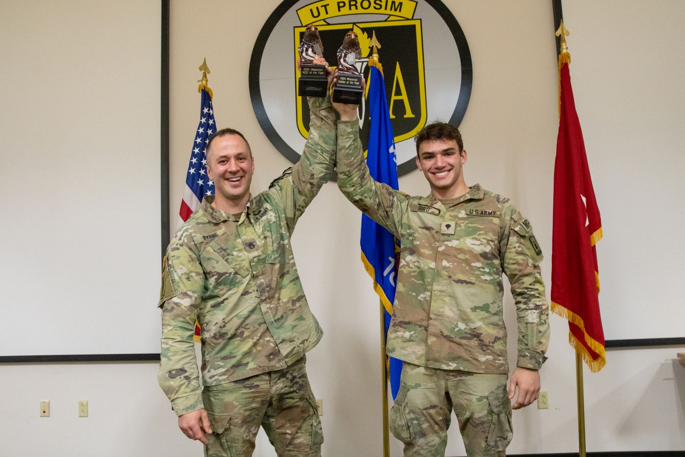 Staff Sgt. Brandon M. Byrne (left), a recruiting and retention non-commissioned officer with Alpha Company, Recruiting and Retention Battalion, and Spc. Vincent A. Bird (right), a military police officer with the 32nd Military Police Company, revel in their victory with their trophies after being named as the 2025 Wisconsin Army National Guard Best NCO and Soldier of the Year respectively during a ceremony held at Fort McCoy, Wis., March 9, 2025. The State Best Warrior Competition is an annual event where participants compete in various warrior skill challenges, including weapons proficiency, land navigation, physical fitness tests, combat first aid, tactical maneuvers, communications, and professional development exercises. (U.S. Army National Guard photo by Sgt. Cesar Salazar Jr.)